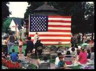 Political speech on town green with american flag in background